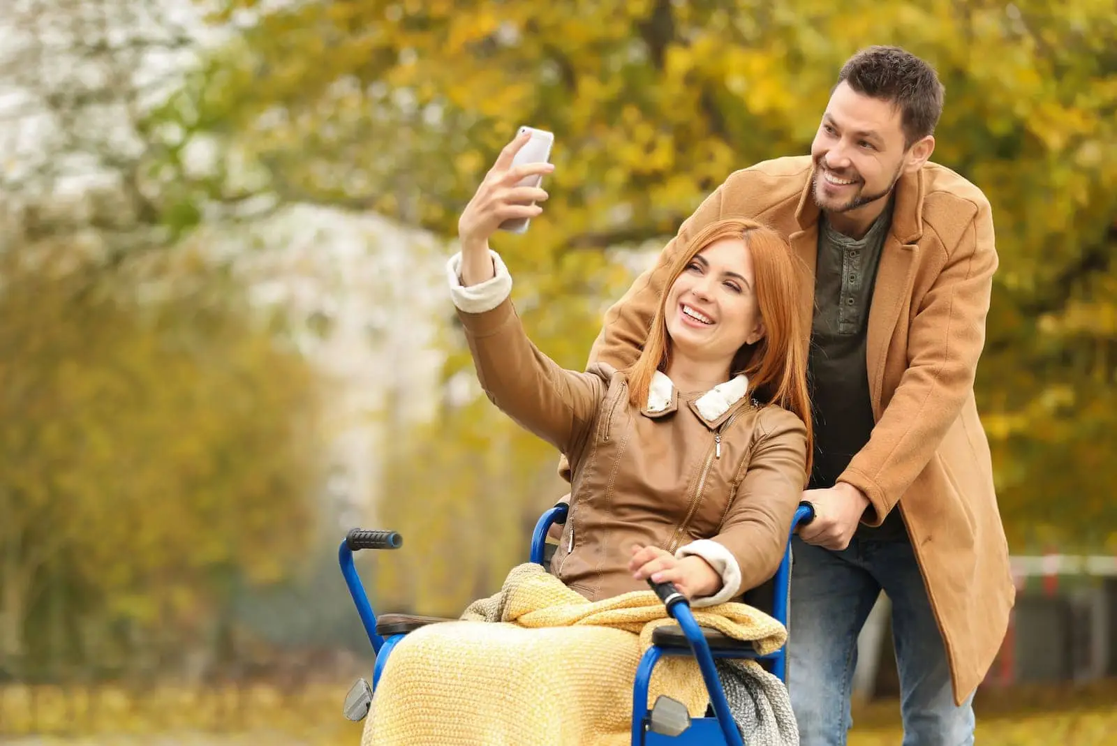Paar macht ein Selfie beim Herbstspaziergang im Park, sie im Rollstuhl